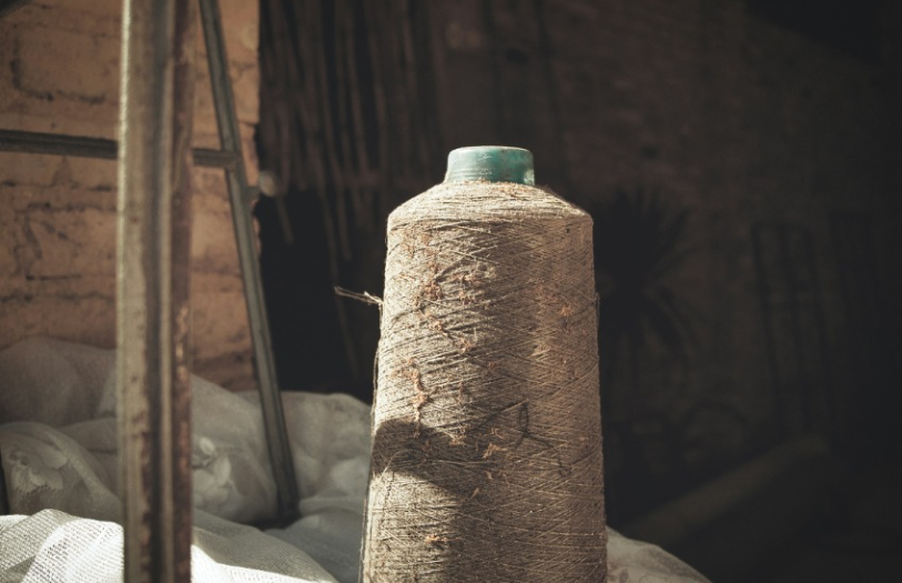 Large spool of thread or twine with a green top in a dimly lit textile workshop setting.