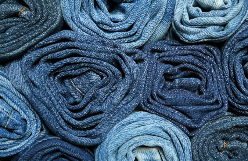 Close-up of multiple rolls of denim jeans in various shades of blue stacked together.