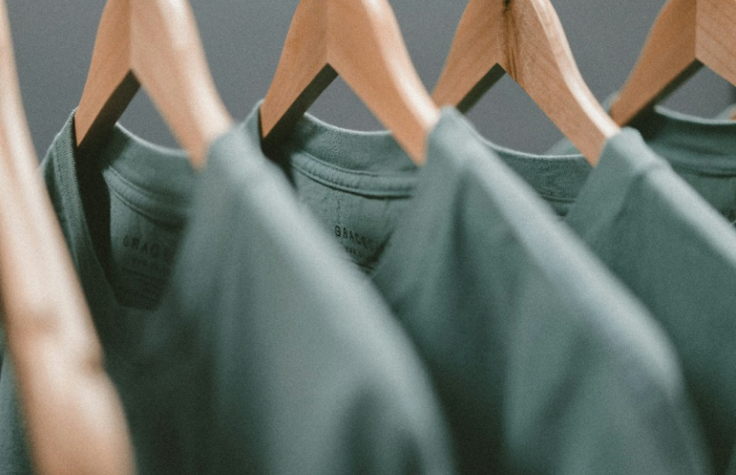 Row of green shirts hanging on wooden hangers against a gray background.