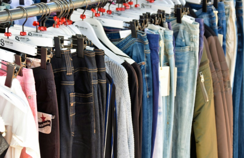 Various pants and jeans hanging on white and black hangers on a metal clothing rack.