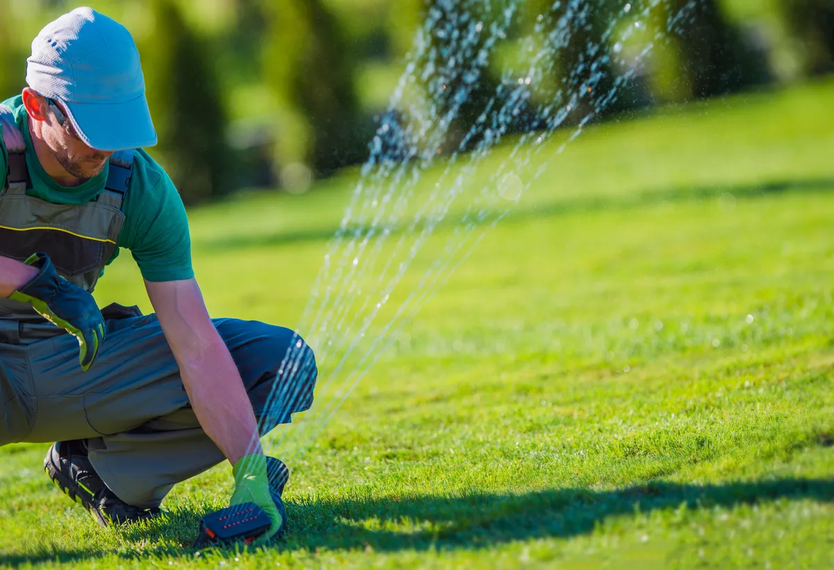 A 4-10 Sprinklers technician servicing an in-ground lawn sprinkler head