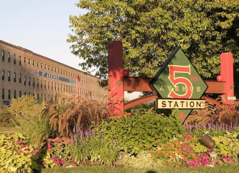 An outdoor, with a brick building, tree, and a sign that reads 5th Avenue Station.