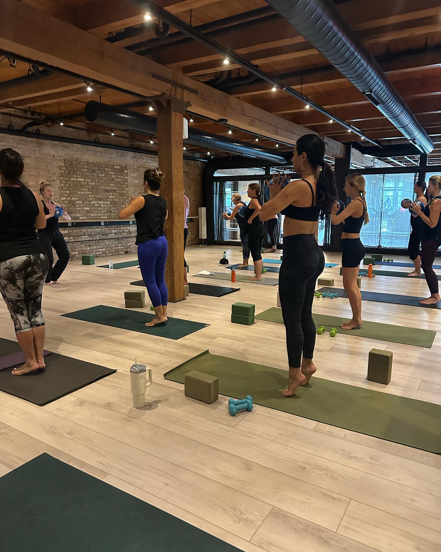 Group of women in a yoga studio standing on mats holding weights in a fitness class.
