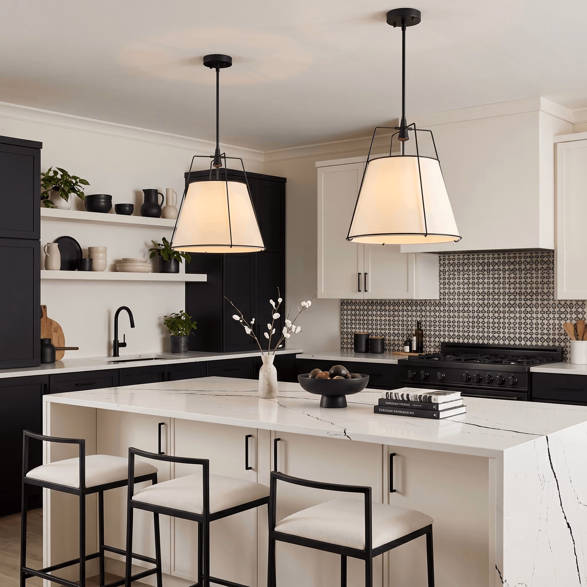 Modern kitchen with black and white cabinetry, a large white marble island with black metal frame stools, two pendant lights, patterned backsplash, and decorative items including a vase with branches and a bowl with fruit on the island.