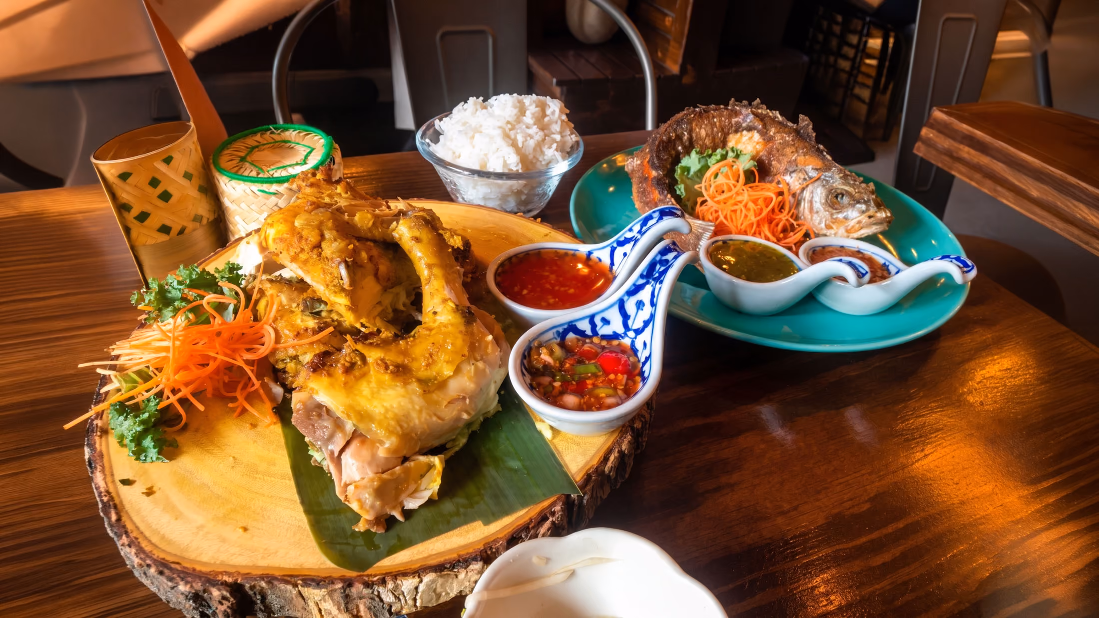 Served grilled chicken, whole fried fish with sauces, rice, and carved carrot garnish on a wooden table.