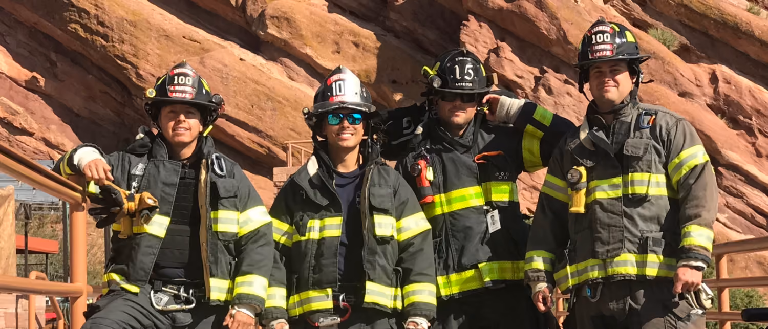 Four firefighters in gear posing outdoors with rocky cliffs in the background.