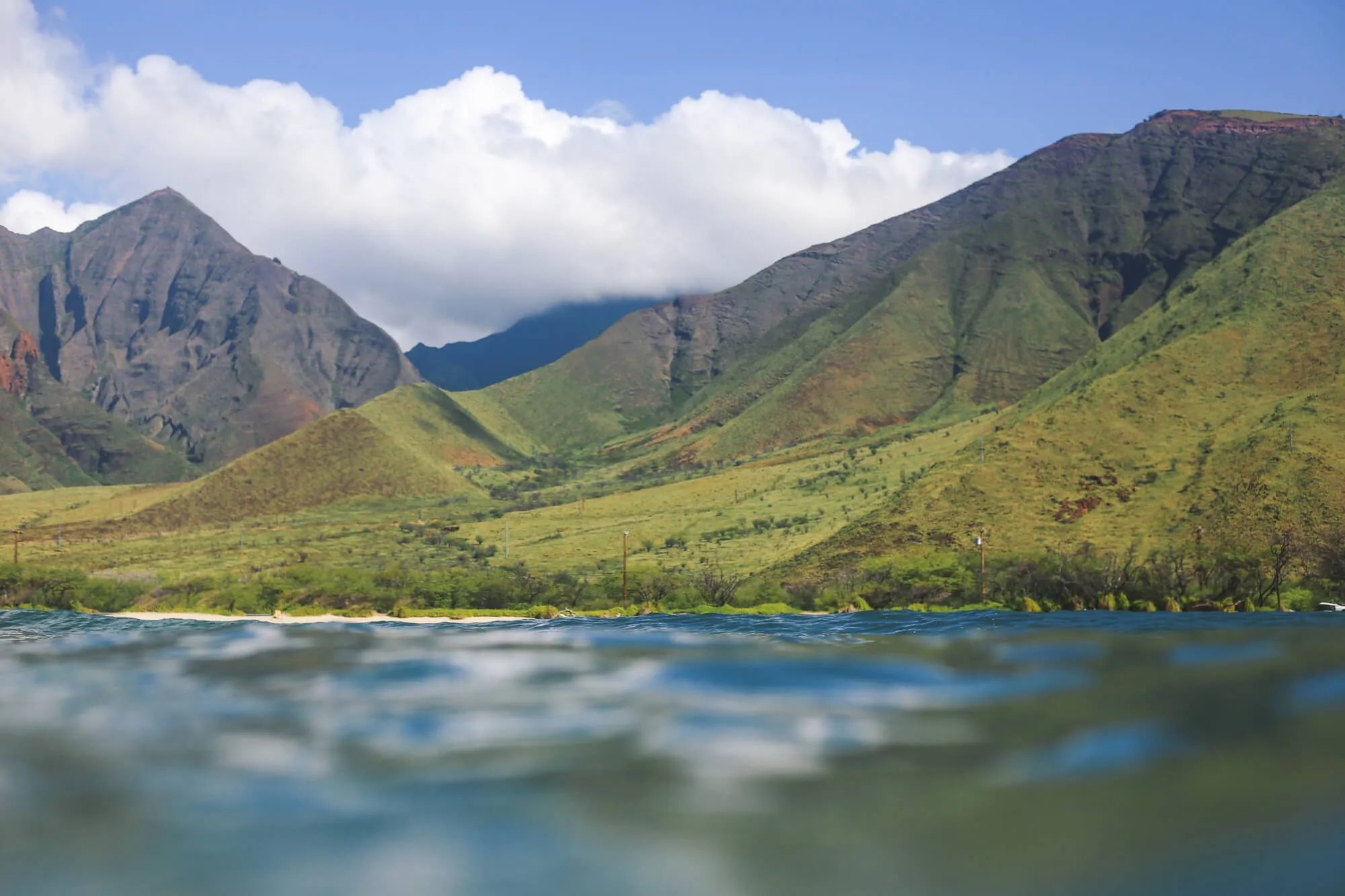 huge green mountains of maui coast and clouds in sky viewed from an ocean perspective