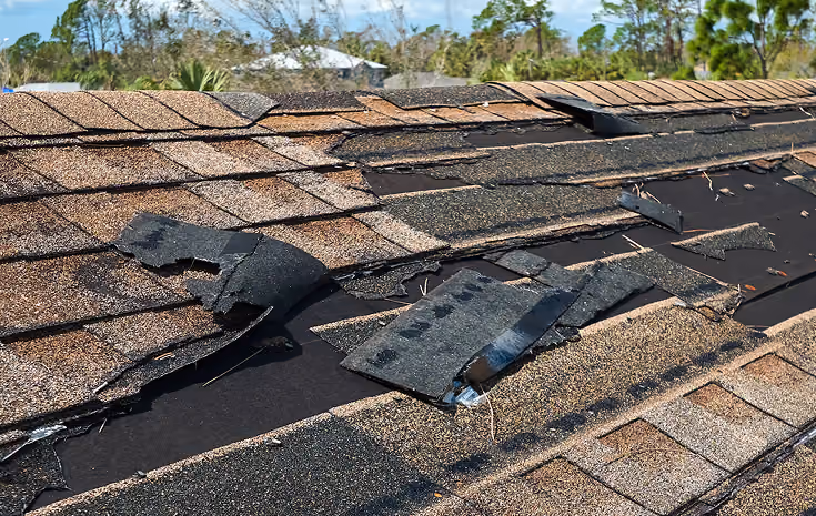 Damaged house roof with missing shingles after storm damage.