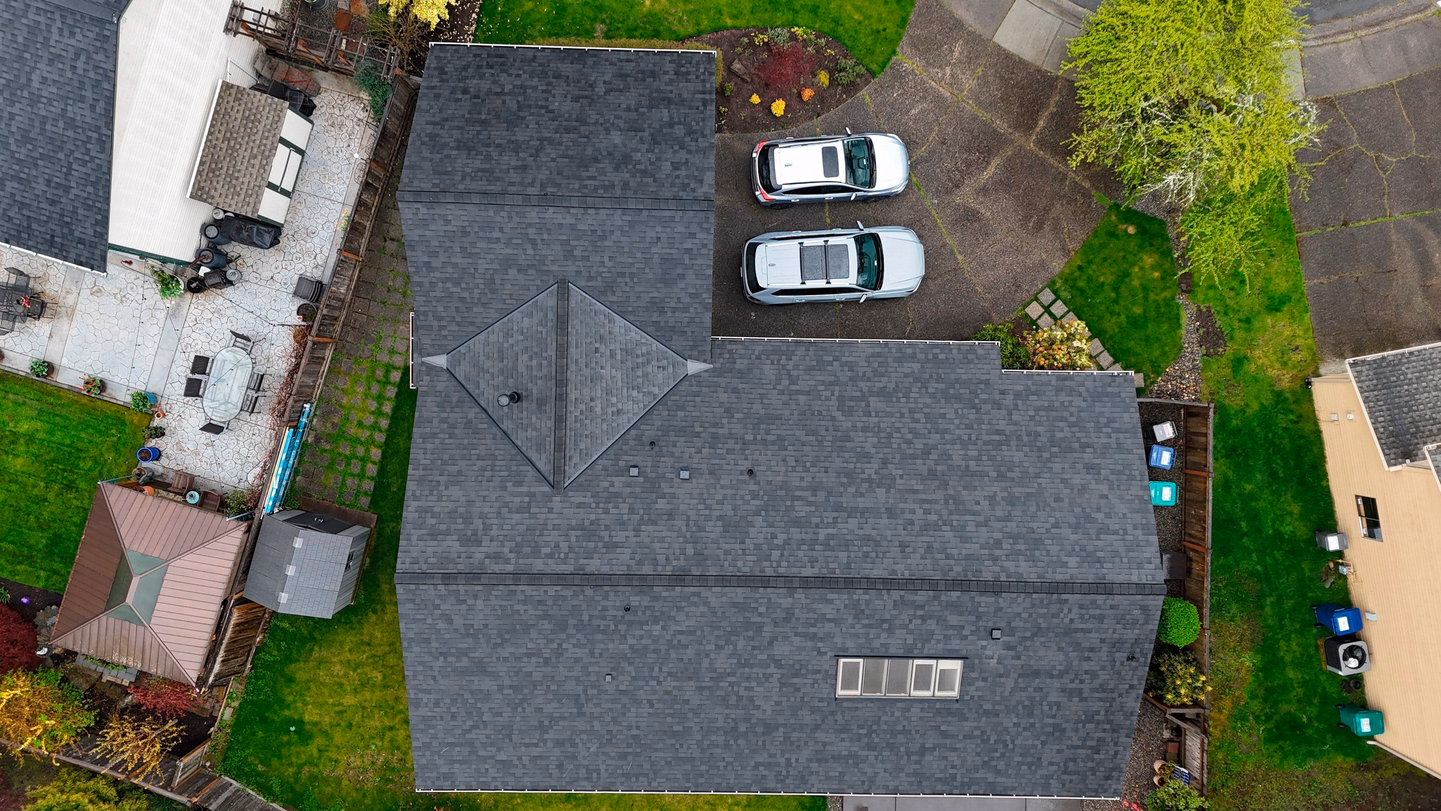 Aerial view of a gray-shingled house roof with two parked silver cars in the driveway.