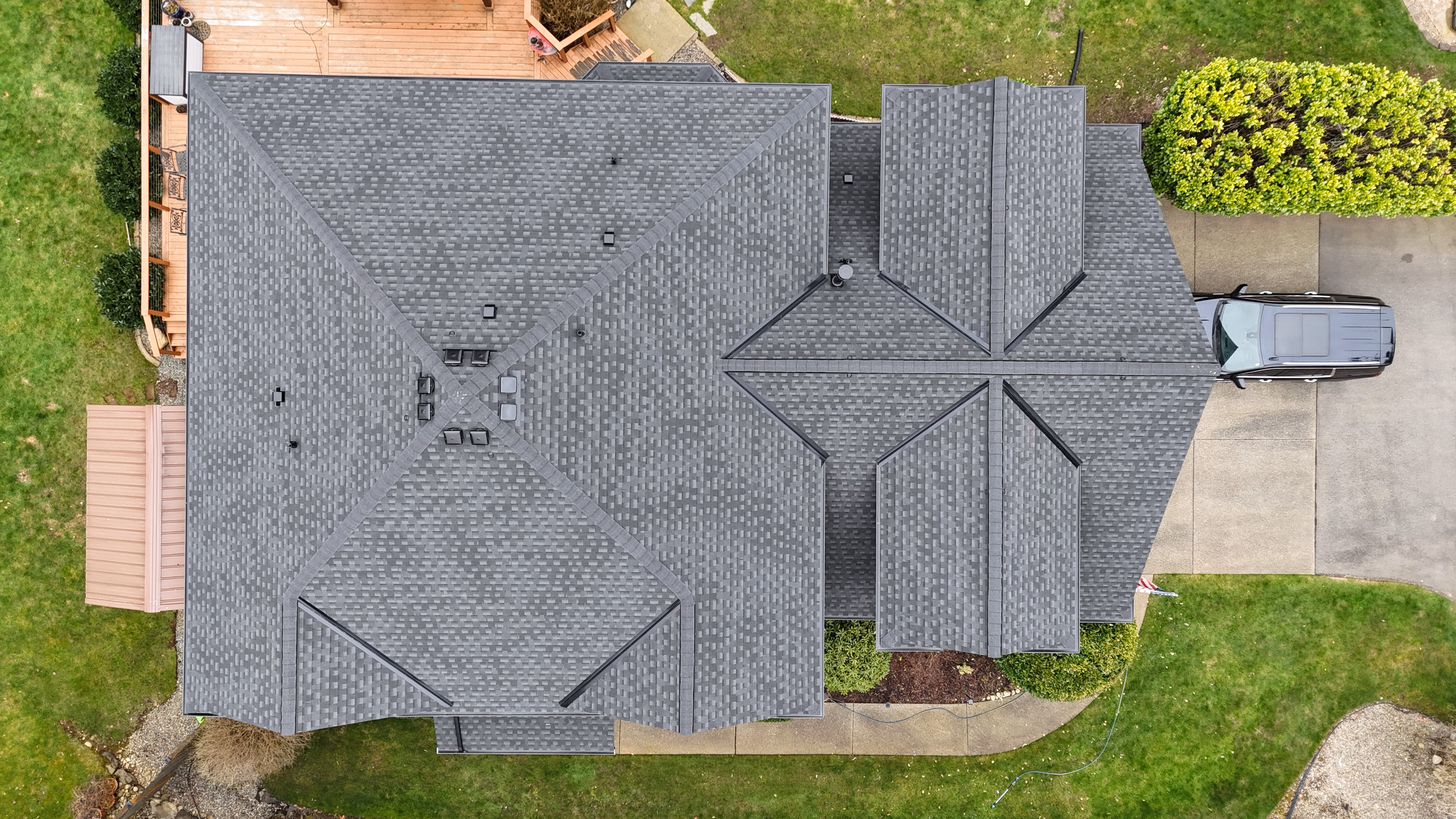 Aerial view of a house with a large gray shingle roof and a car parked in the driveway.