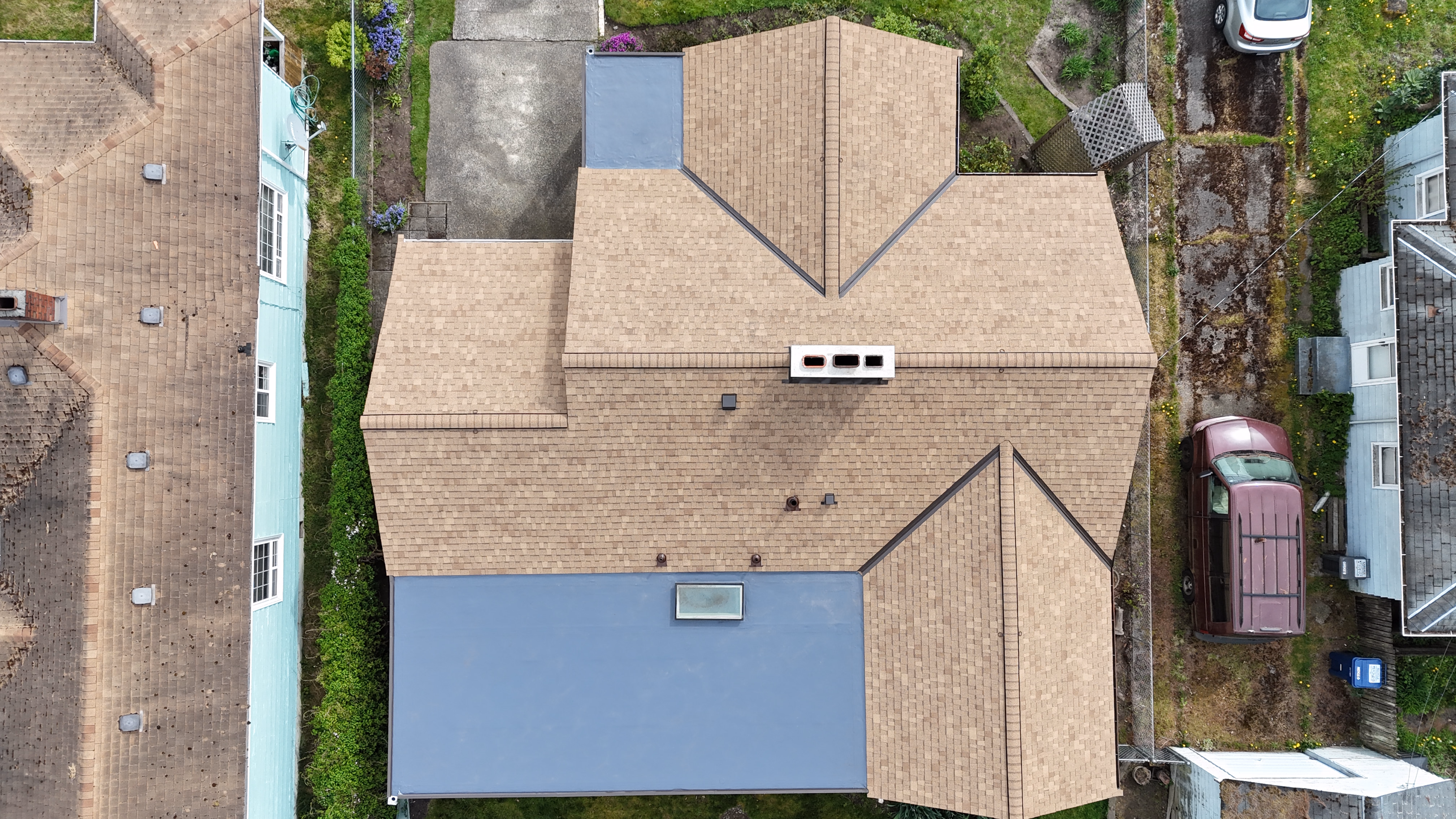 Aerial view of a large beige roof with a blue extension and surrounding houses and cars.