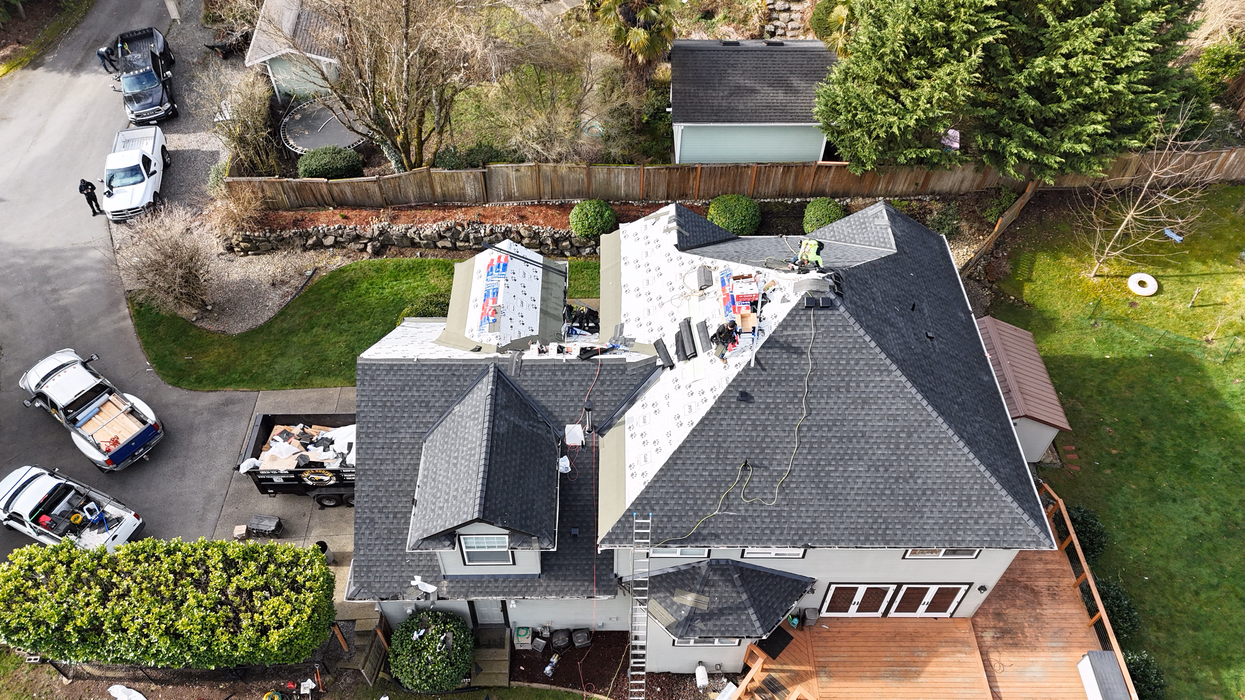 Aerial view of a house with workers installing new shingles on the roof during roofing project.