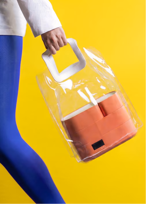 Person holding a transparent bag with orange containers against a bright yellow background.