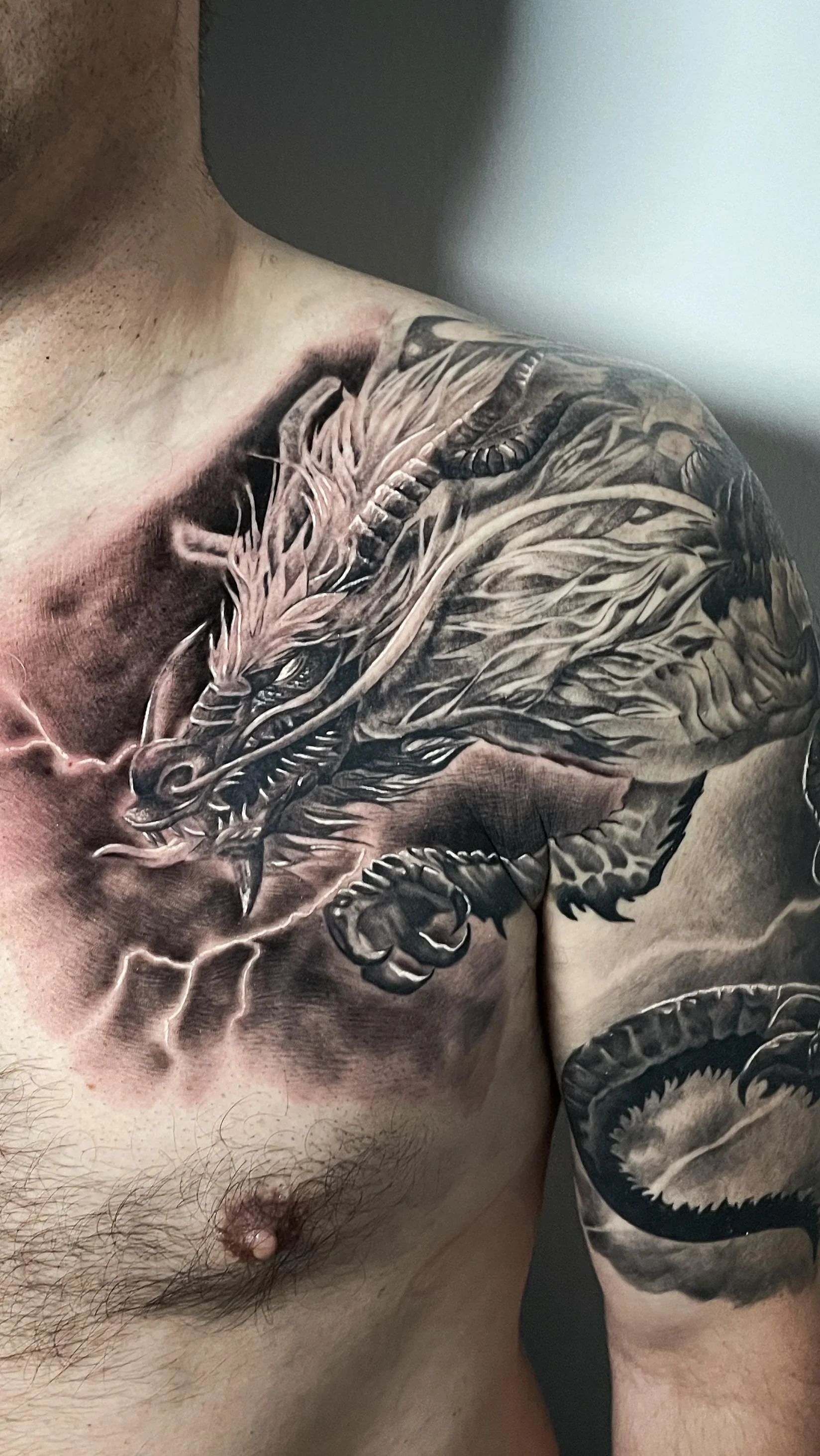 Realistisches Black and Grey Drachen Tattoo an Brust, Schulter und Oberarm – asiatischer Drache mit Blitzen, INK SOCIETY