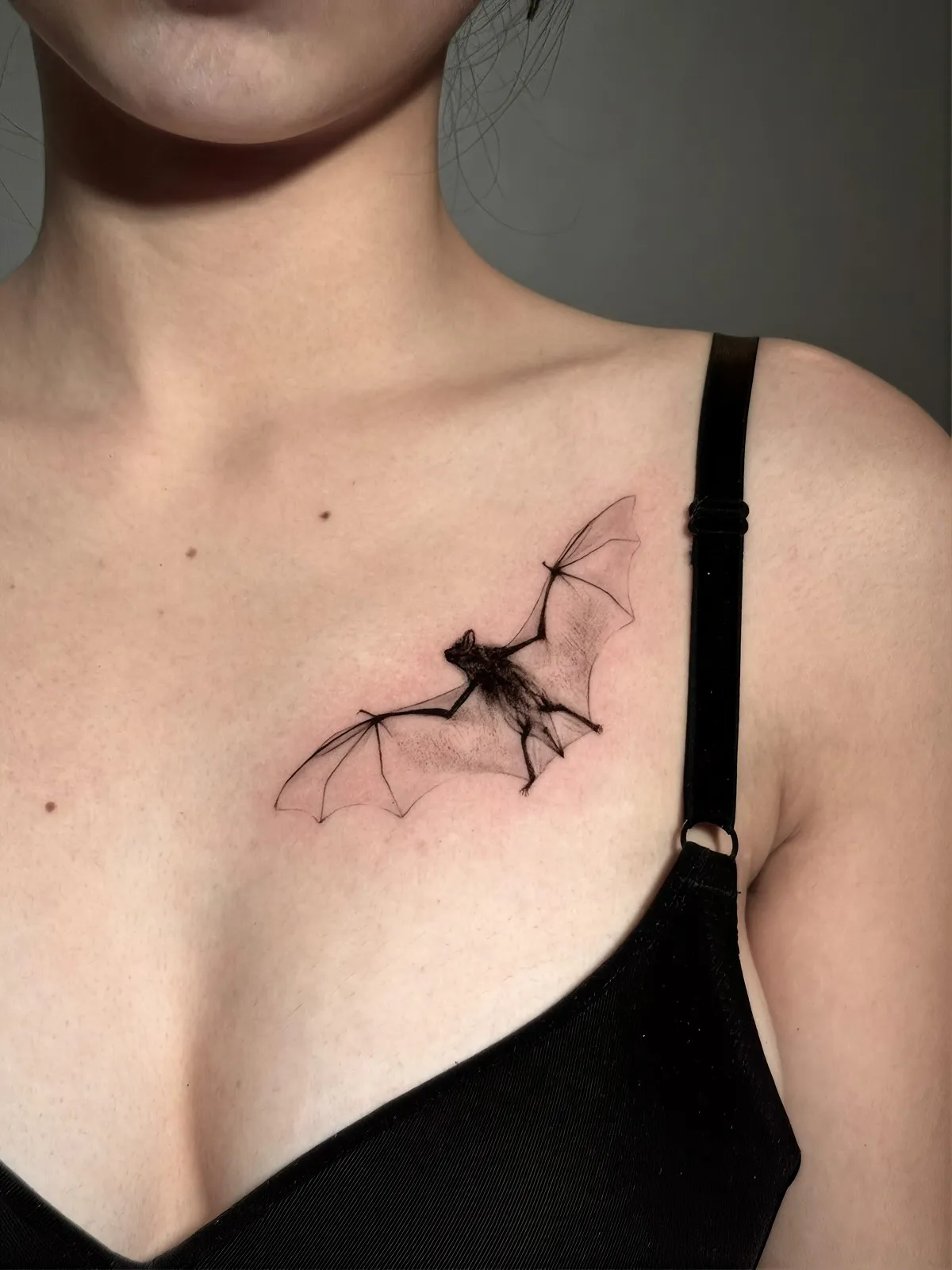 Fledermaus Tattoo unter dem Schlüsselbein – fliegende Fledermaus mit transparenten Flügeln in Fine Line und Black and Grey, von Lara, INK SOCIETY