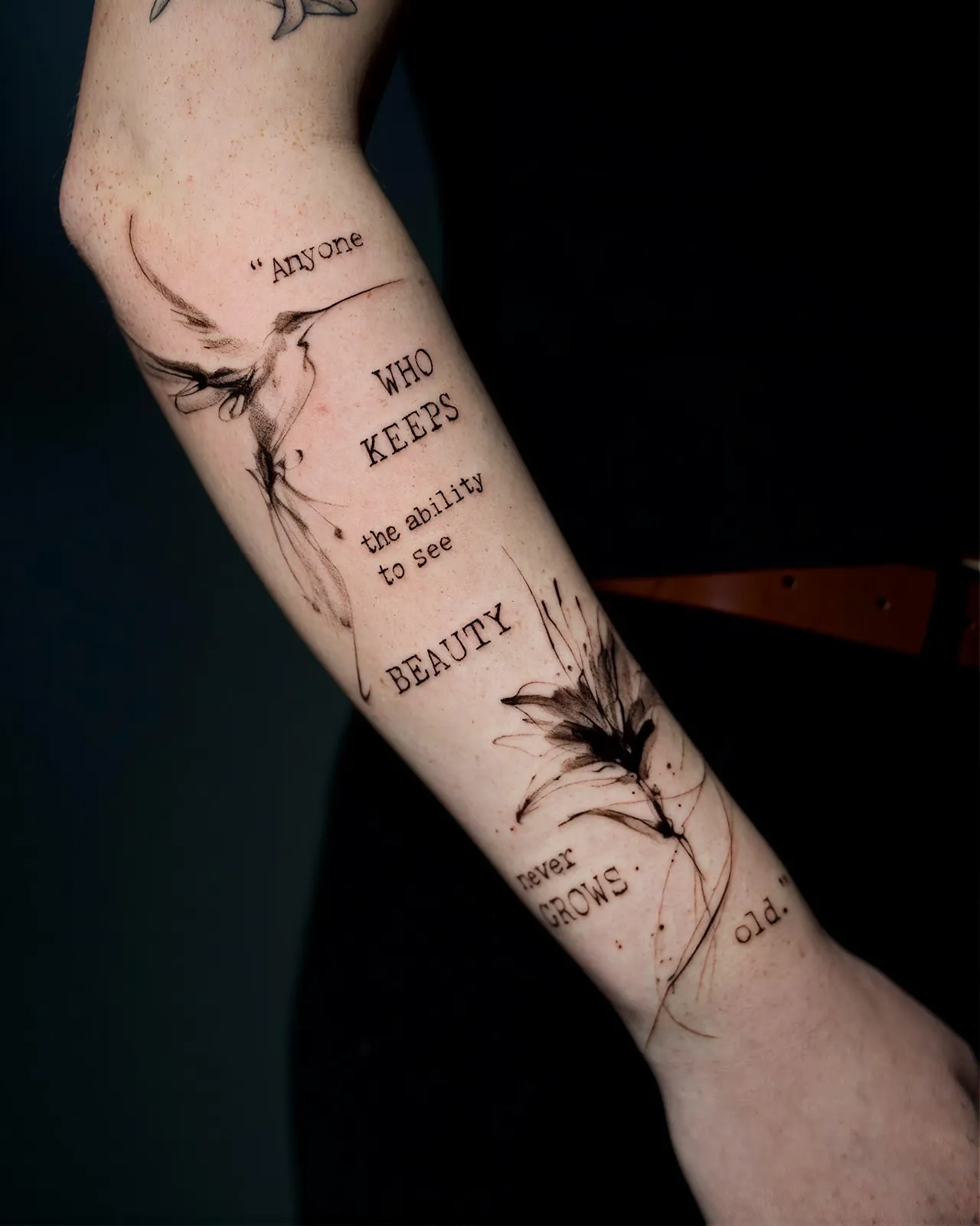 Schriftzug Tattoo am Unterarm – Zitat „Anyone who keeps the ability to see beauty never grows old“ in Schreibmaschinenschrift mit Kolibri und Blüte im Sketch-Stil, von Lara, INK SOCIETY