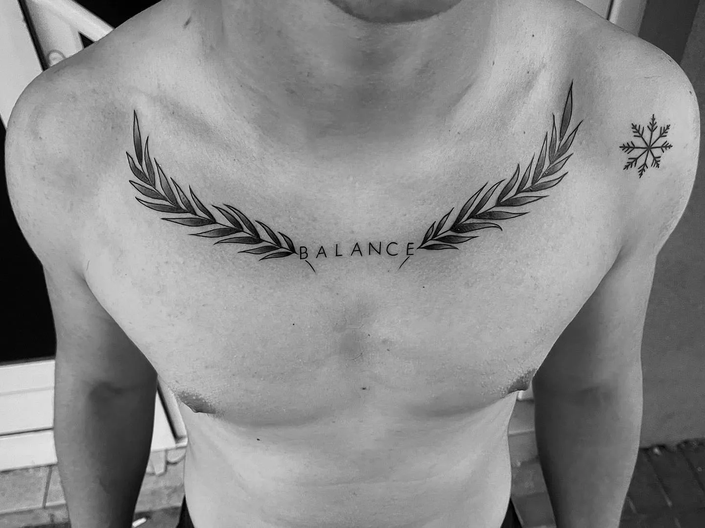 Fine Line Schriftzug Tattoo auf der Brust: „BALANCE“ zwischen zwei Blätterzweigen am Schlüsselbein, dazu kleine Schneeflocke an der Schulter, von Gojko, INK SOCIETY