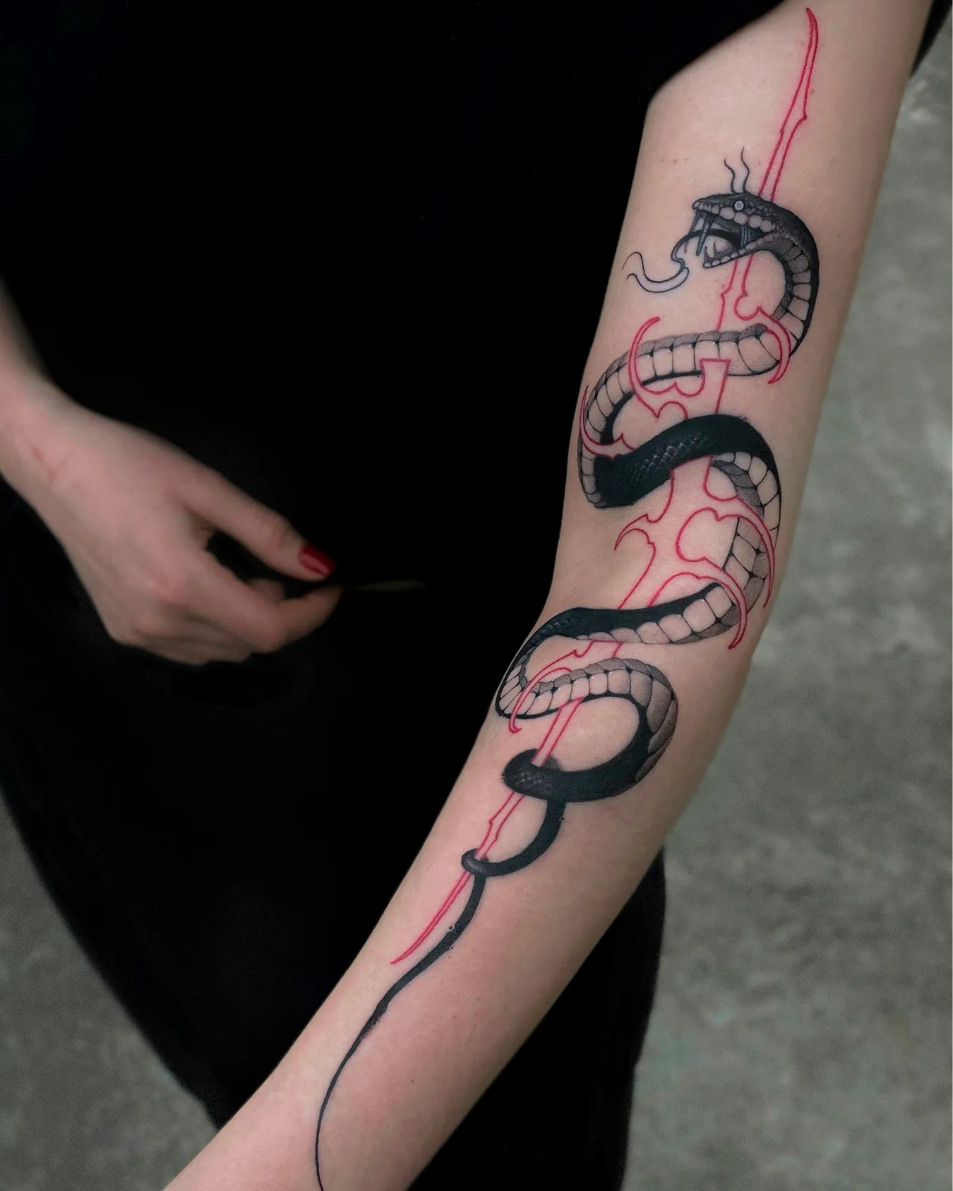 Schlangen-Tattoo am Arm mit schwarzer Schlange um ein rotes Neo-Tribal-Schwert, gestochen von Asti im Tattoostudio in Kiel
