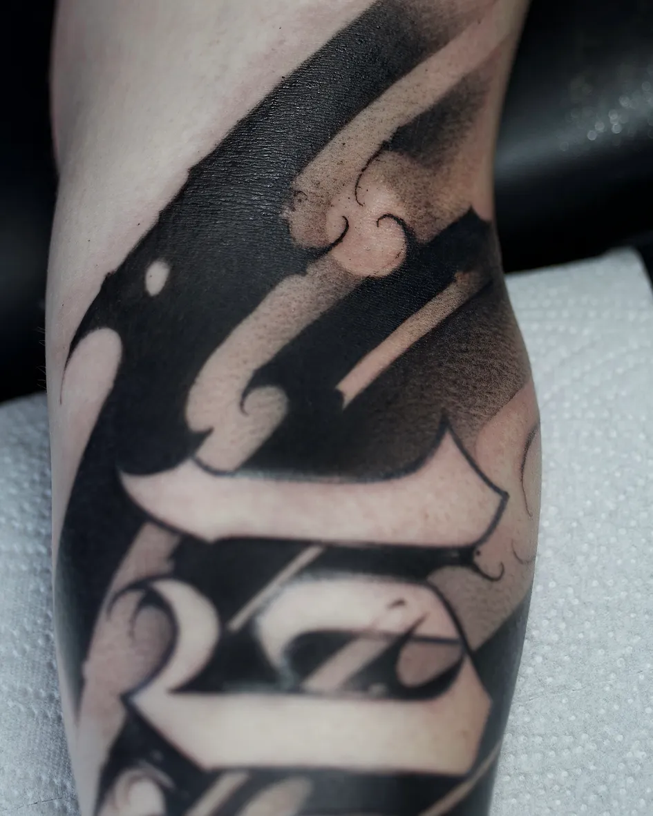 Lettering-Tattoo am Arm mit großen, gebrochenen Buchstaben, ausgespart aus sattem Schwarz, gestochen von Asti bei INK SOCIETY in Kiel