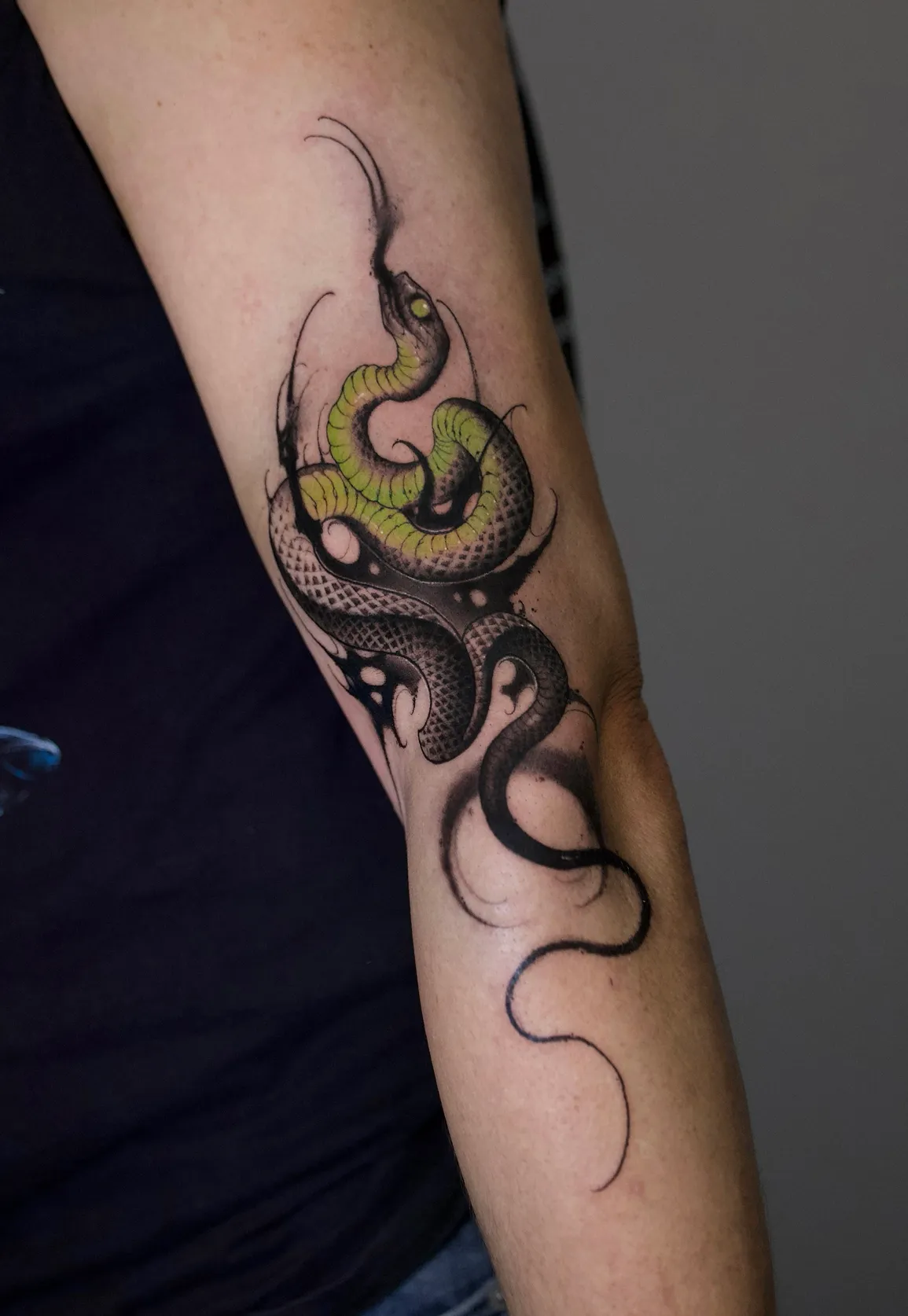 Python-Tattoo am Arm: grüne Python mit dunklen Schuppen und schwarzen Neo-Tribal-Formen, gestochen von Asti im Tattoostudio in Kiel