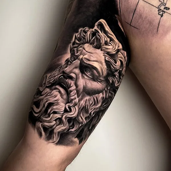 Black & Grey Realistic Tattoo am Oberarm: bärtiger Kopf einer antiken Götterstatue, gestochen von Gojko bei INK SOCIETY in Kiel