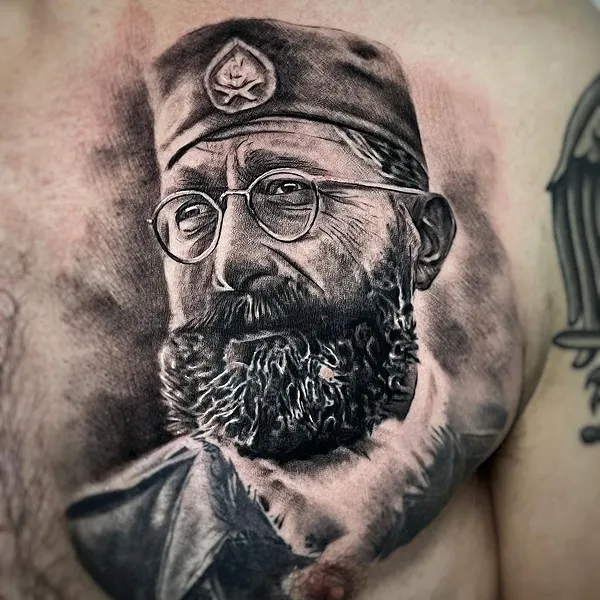 Realistisches Black and Grey Portrait Tattoo auf der Brust – Mann mit Vollbart, Nickelbrille und Militärmütze, INK SOCIETY