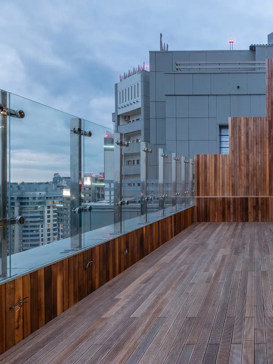 Moderne Dachterrasse mit Glasgeländer und Holzverkleidung in einer Stadt bei bewölktem Himmel.