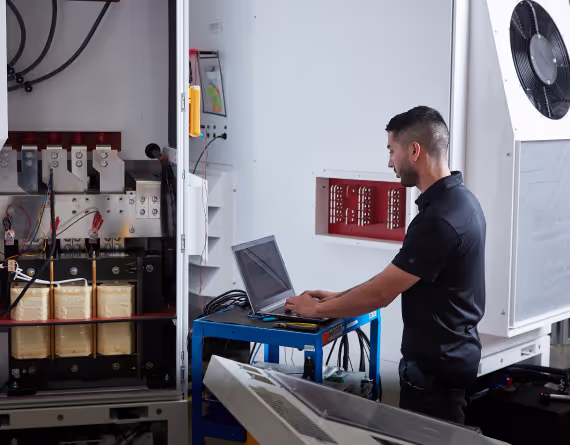 Technician configuring an EPC Power unit on a laptop beside open control cabinet wiring.