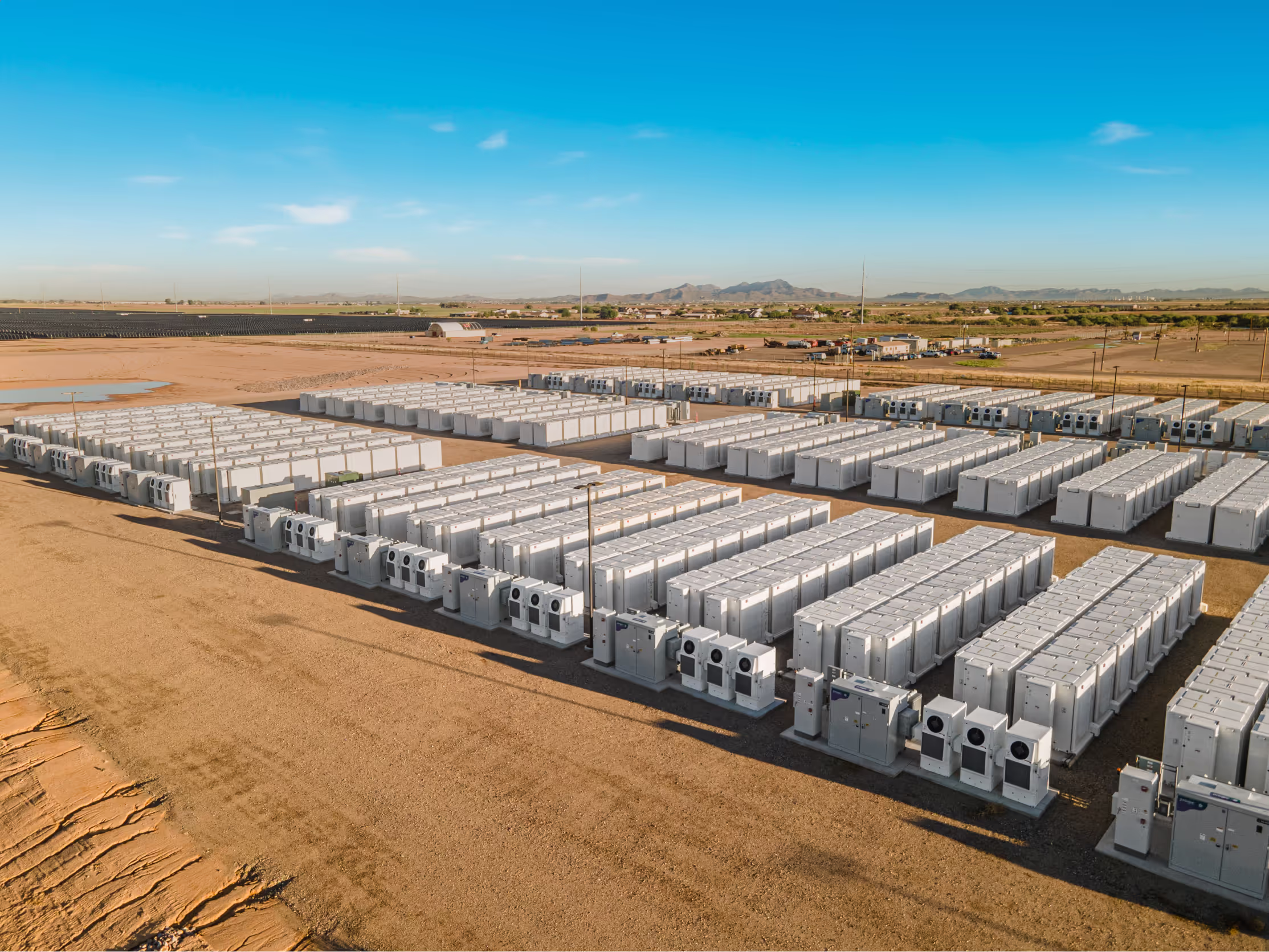 Large array of white industrial battery storage units in a desert landscape under a blue sky.