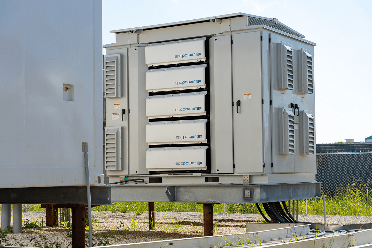 EPC Power M System unit elevated on steel piers at a fenced site, angled view of front and side panels.