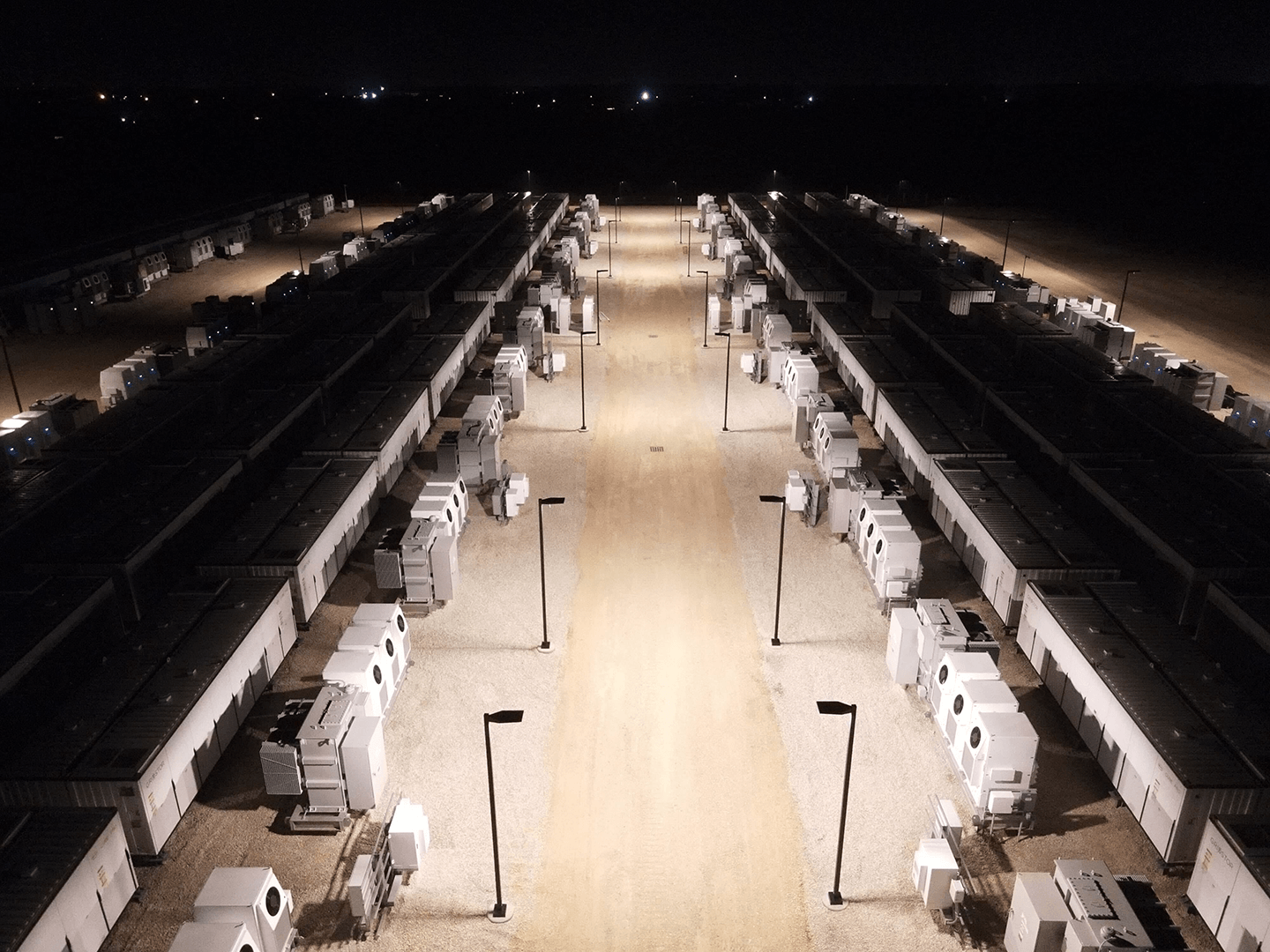 Aerial night view of a large battery energy storage site with long rows of containers.
