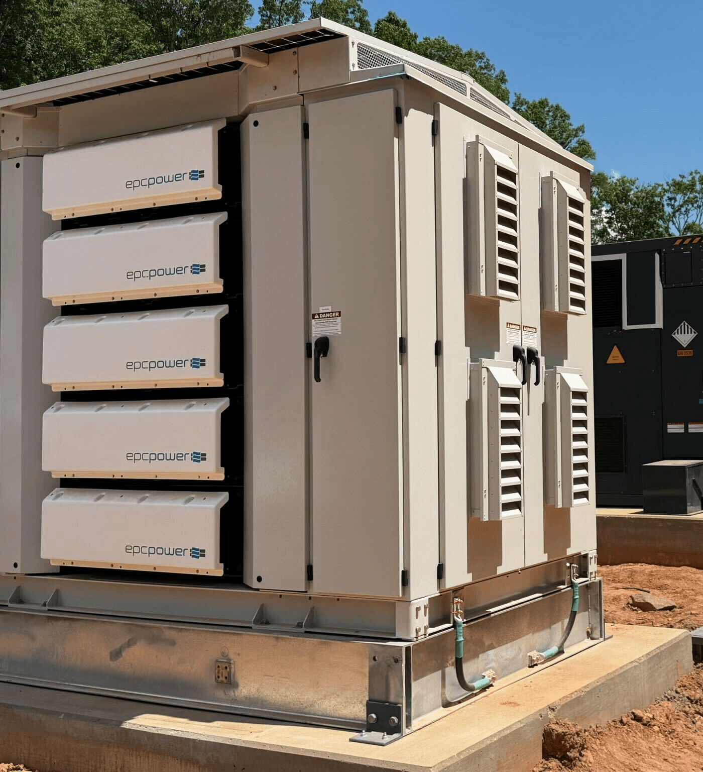 EPC Power M System unit at a job site, angled view of front modules and side vents with a generator in the background.