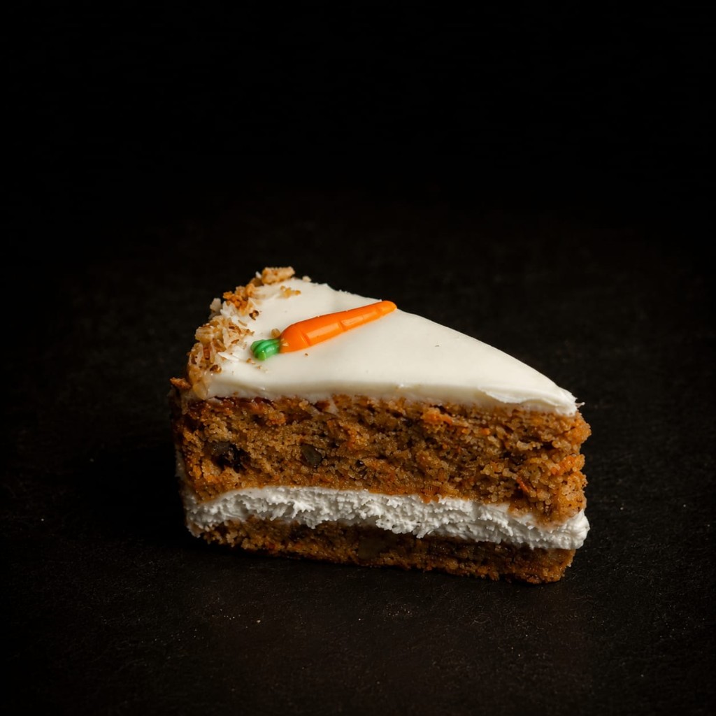 Stück Karottentorte mit Frischkäsecreme und Marzipankarotte.