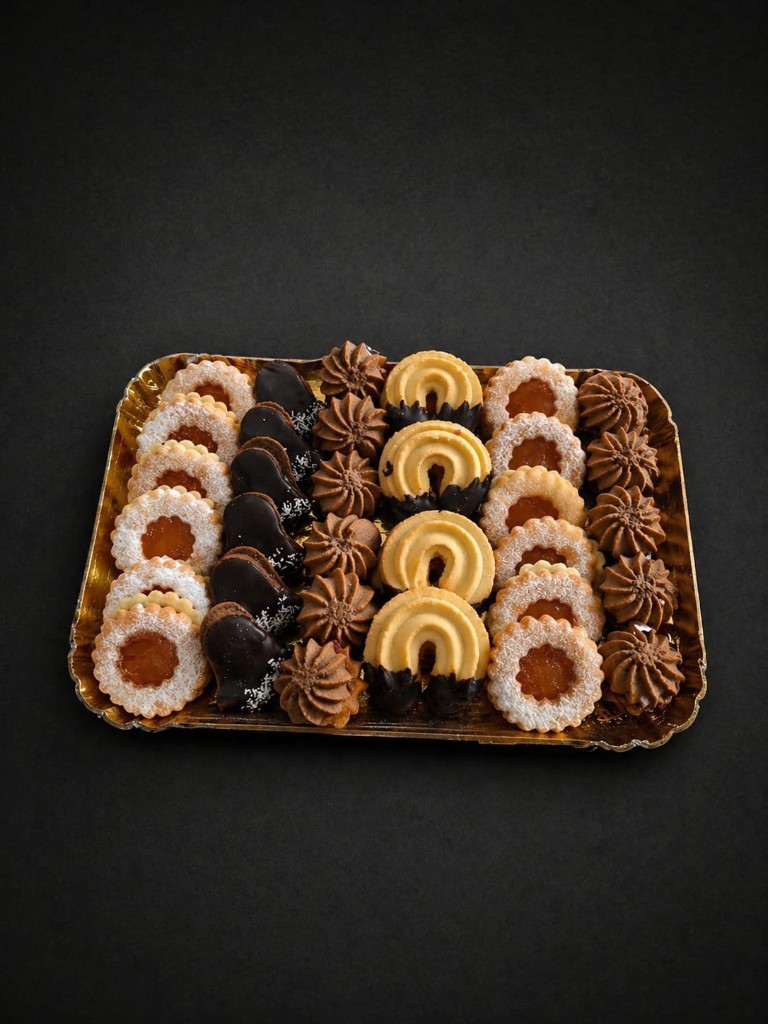 Butter-Teebäckerei mit Linzer Augen, Schokoherzen und Hufeisen auf goldenem Tablett.