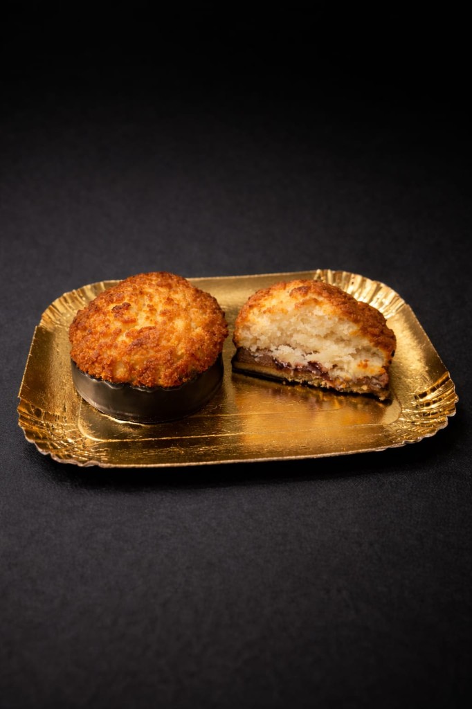Kokoskuppeln mit gerösteter Kokoskruste und Schokoladenboden auf goldenem Tablett.