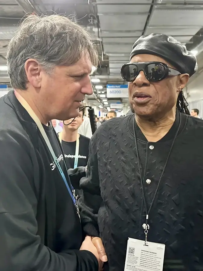 Glidance CEO Amos Miller and renowned musician Stevie Wonder sharing a friendly handshake at the CES 2024 conference.