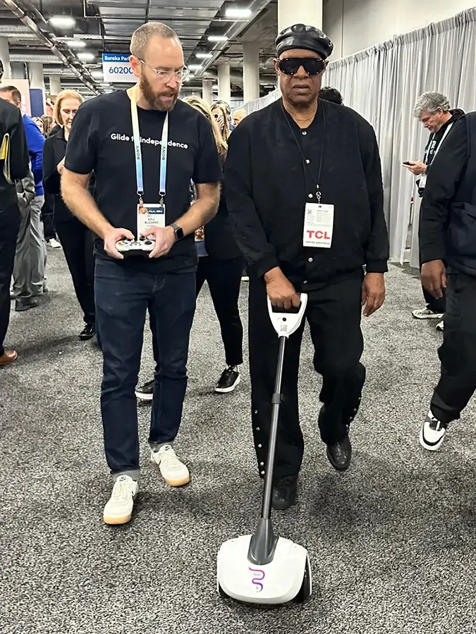 A Glidance employee assisting Stevie Wonder in demonstrate the Glide technology at CES 2024, showcasing the accessibility and user-friendly features of the product.