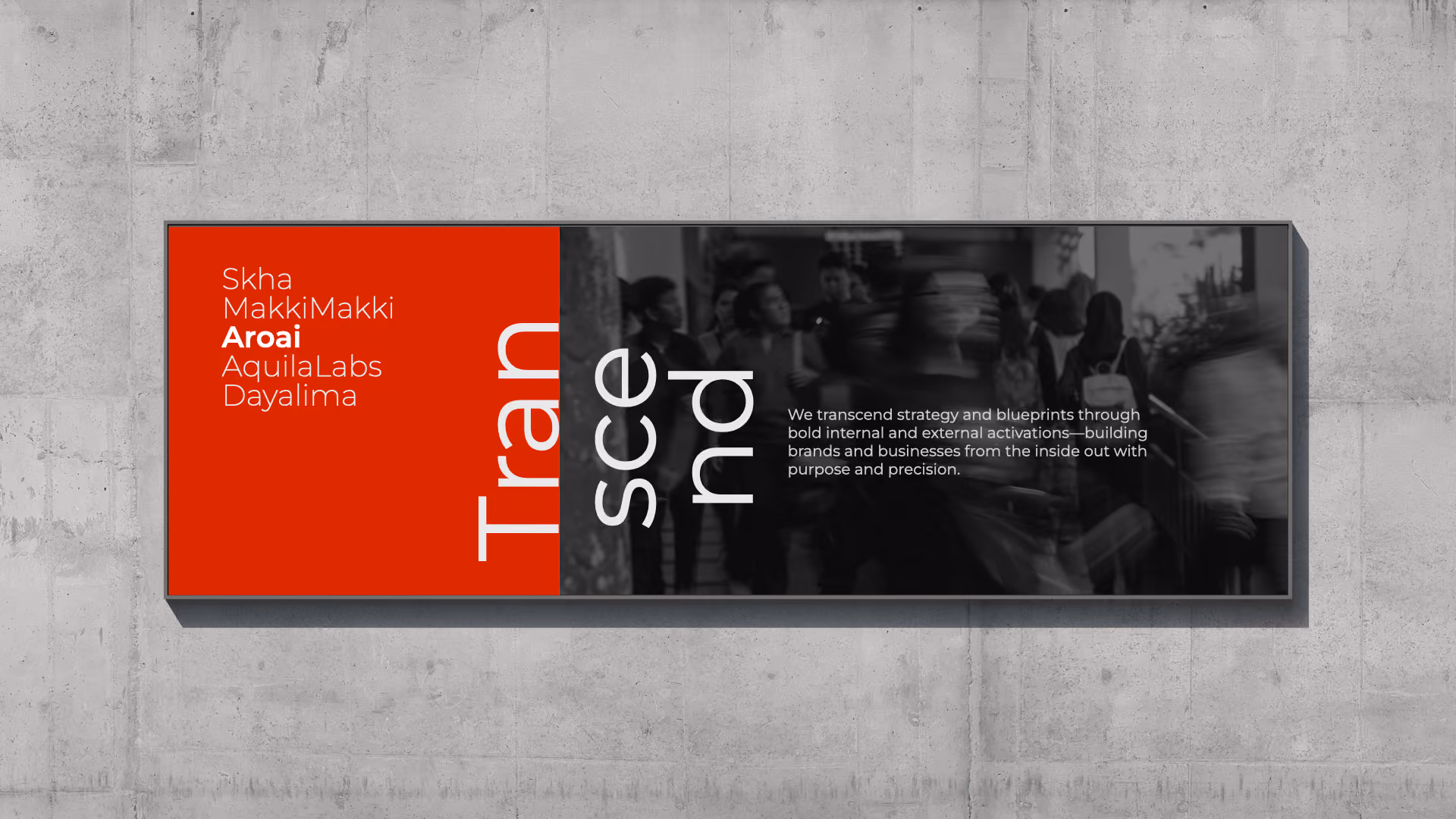 Wall-mounted rectangular digital display with a red section listing names 'Skha, MakkiMakki, Aroai, AquilaLabs, Dayalima' and the word 'Transcend' split vertically in large white letters on a black background. To the right, white text reads: 'We transcend strategy and blueprints through bold internal and external activations—building brands and businesses from the inside out with purpose and precision.' Background shows blurred people walking.