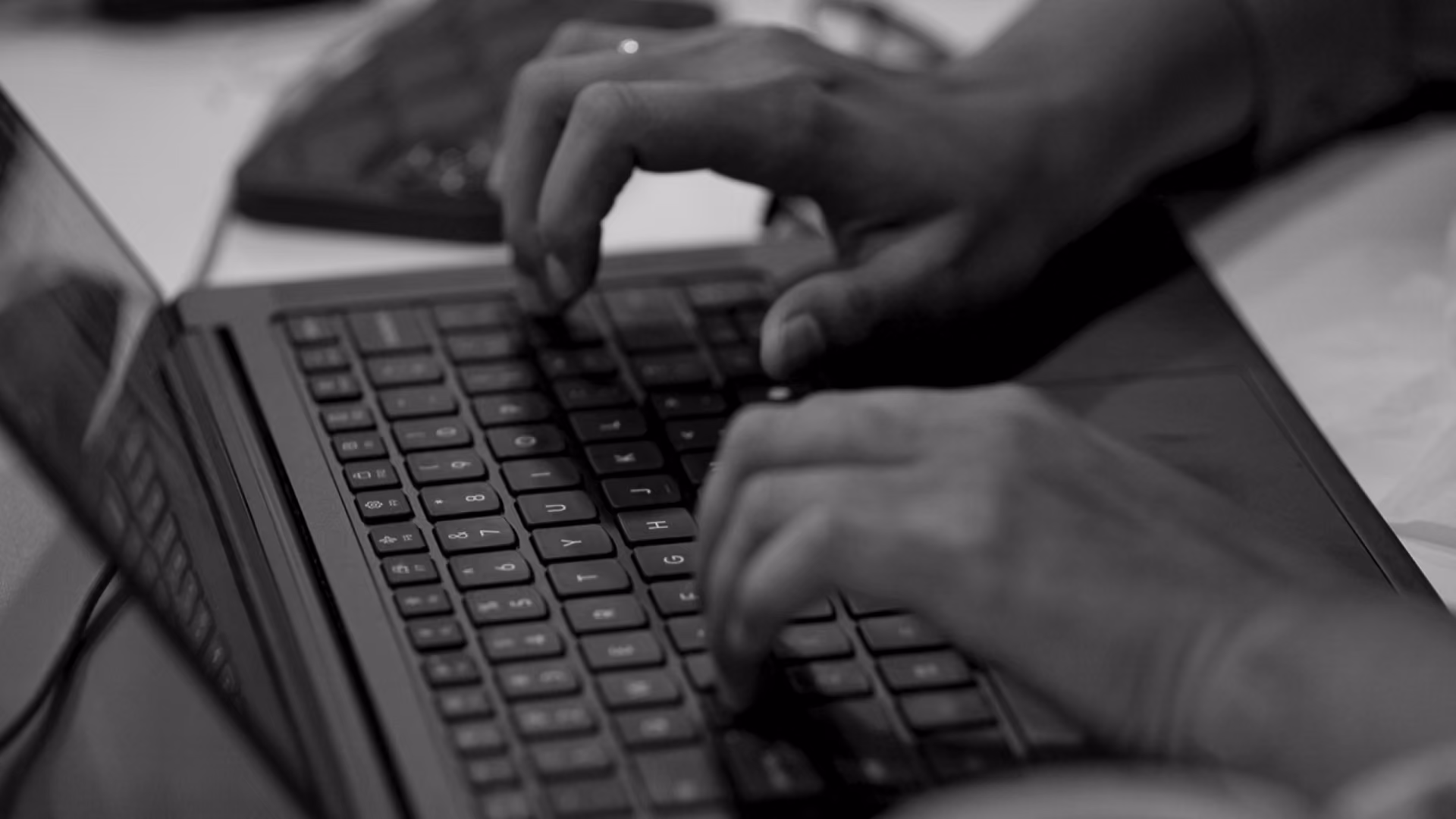 Close-up black and white photo of hands typing on a laptop keyboard.