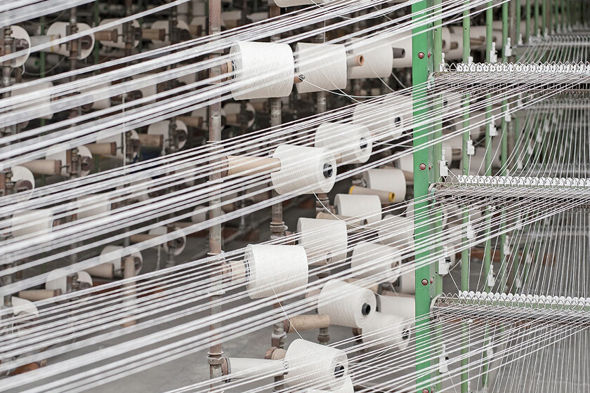 Rows of white yarn spools arranged on a textile machine with threads stretched across the frame.