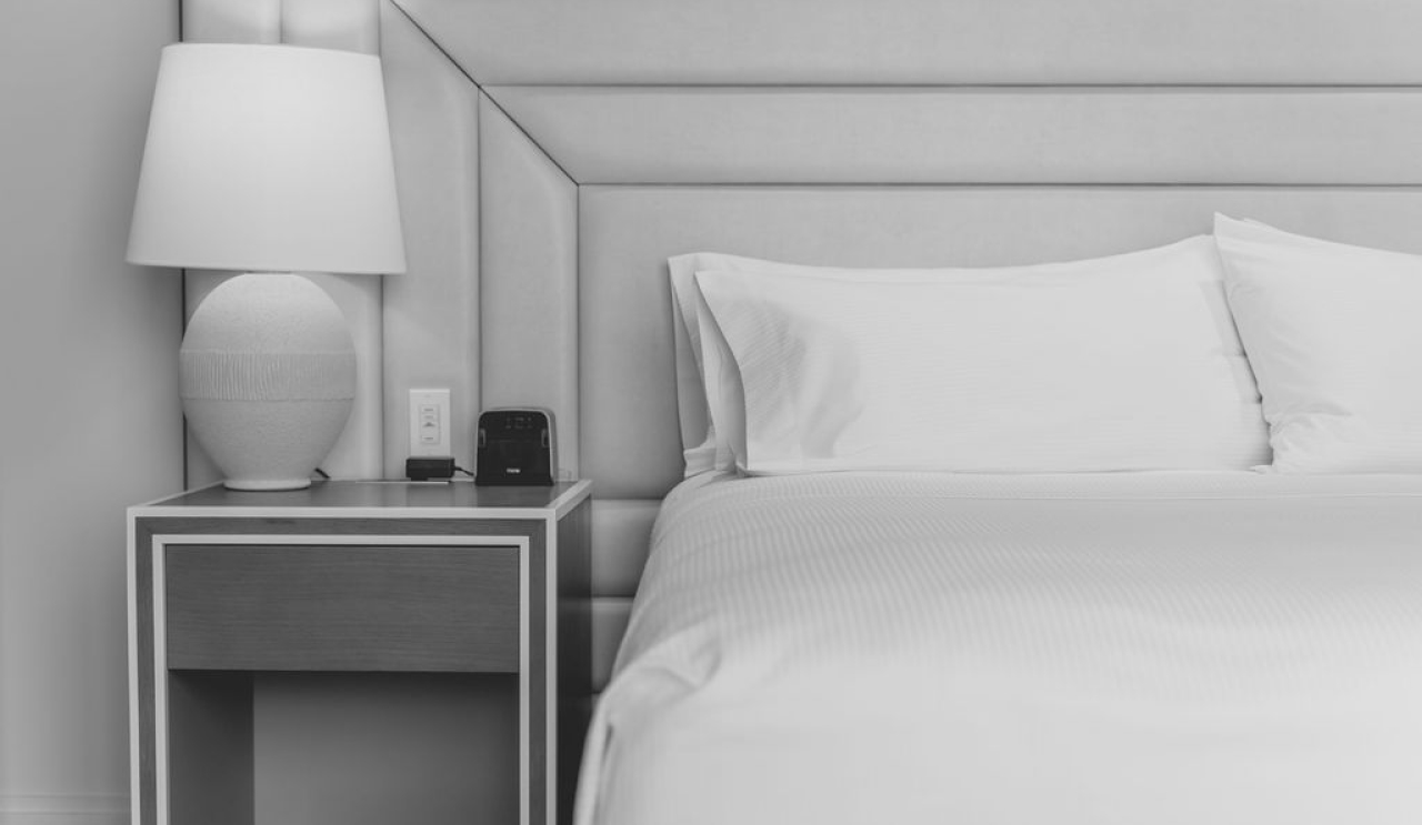 Bed with white pillows and linens next to a bedside table with a lamp and clock.