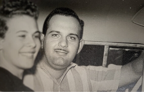 Black and white photo of a smiling man and woman sitting closely, the man looking at the camera.
