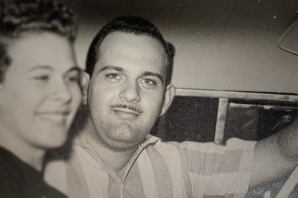 Black and white photo of two smiling men sitting close together.