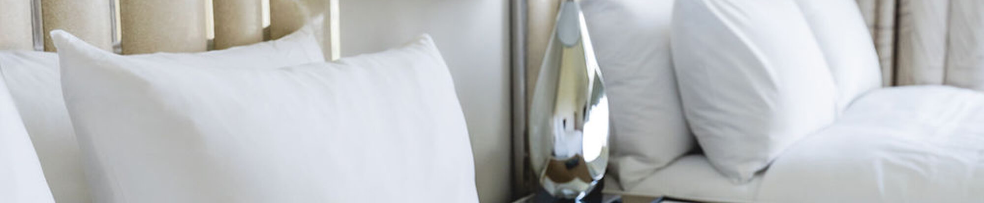 Close-up of a bed with multiple white pillows and a metallic teardrop-shaped bedside lamp.