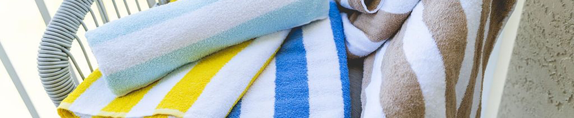 Close-up of colorful striped towels draped over a light blue wicker chair near a textured wall.