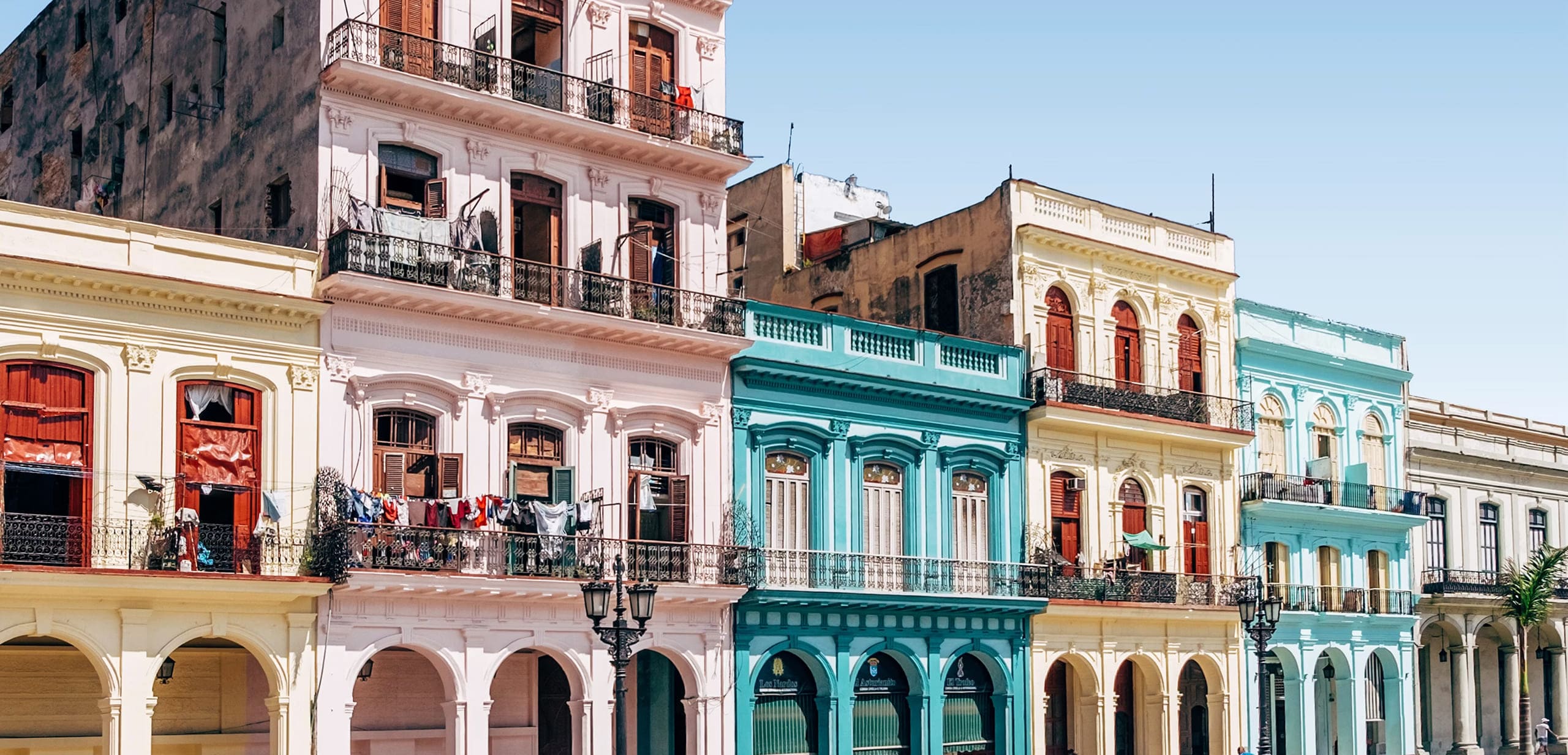 Colorful colonial buildings with balconies and clothes hanging, under a clear blue sky.