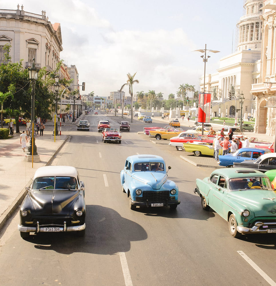 Street in Havana with classic American vintage cars driving and parked near historic buildings.