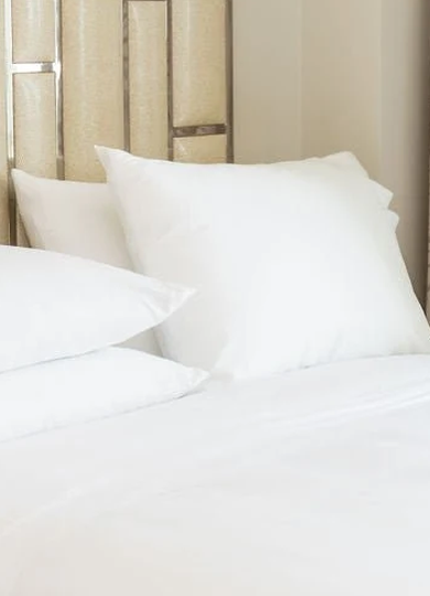 Close-up of a bed with white pillows and white bedding against a beige and gold headboard.