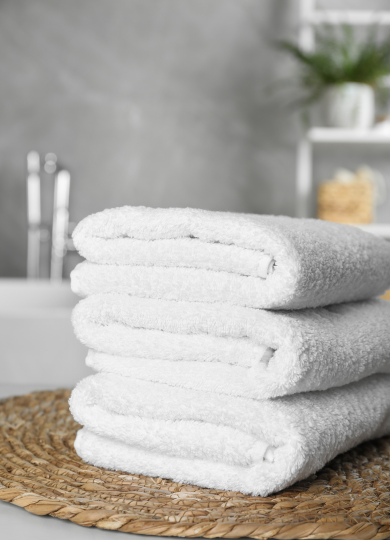 Stack of three neatly folded white towels on a woven mat in a softly lit bathroom.