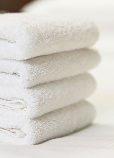 Stack of four neatly folded white towels on a white surface with soft lighting.